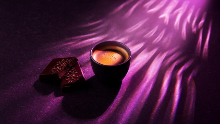 Tableta de chocolate negro partida junto a taza de espresso sobre superficie de piedra violeta oscura con iluminación editorial bioluminiscente, evocando la conexión entre polifenoles del cacao y café con la barrera intestinal y la resistencia a la insulina.